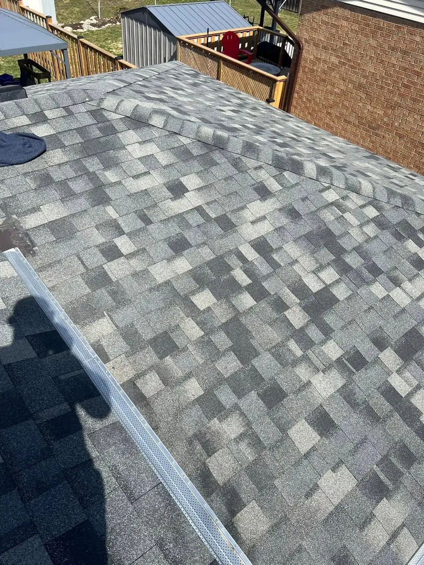 A completed multi-tone grey architectural shingle roof shot down the slope, with a red brick wall and wood deck beyond.