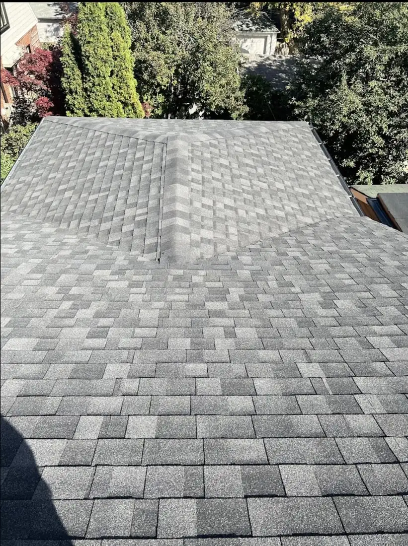 A completed mid-grey architectural shingle hip roof with clean valley and ridge lines, mature cedars filling the background.
