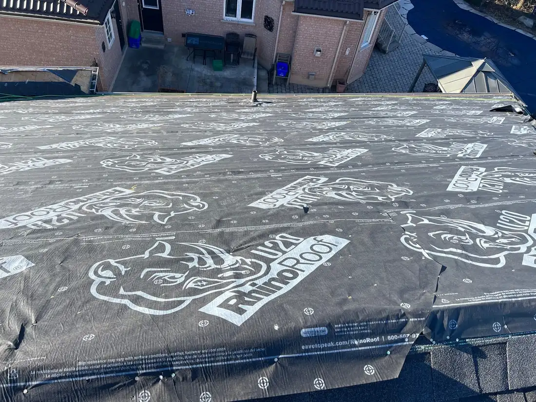 A low-slope roof section fully covered in branded RhinoRoof U20 synthetic underlayment with cap nails in a grid pattern.
