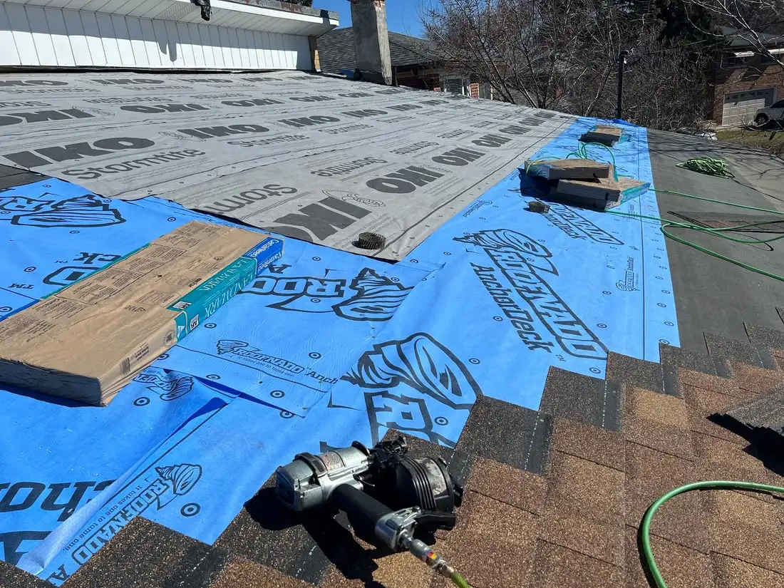 Grey IKO Stormtite ice and water membrane meeting blue Roofnado AnchorDeck underlayment, with a coil nailer and air hose on the deck.