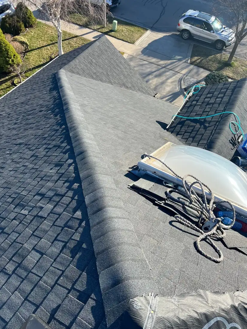 A finished grey roof with a domed skylight in its curb, coiled climbing rope and rigging hardware laid out on the shingles.